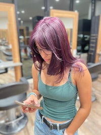 a woman with purple hair looking at her phone in a salon